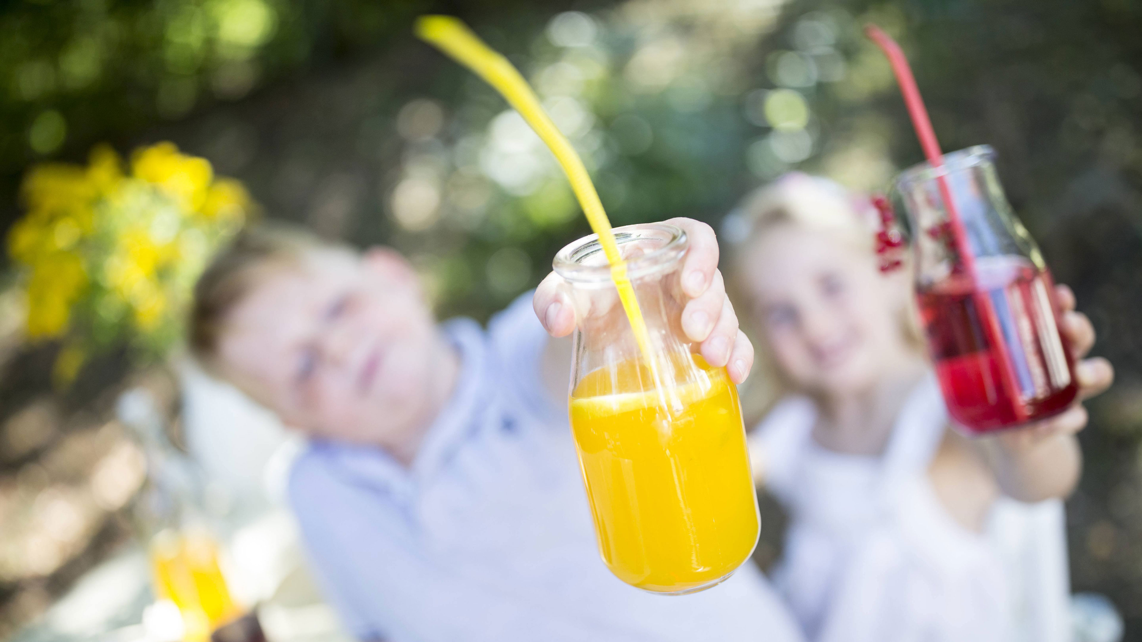 Ein Junge und ein Mädchen halten orangene und rote Limonande in der Hand.