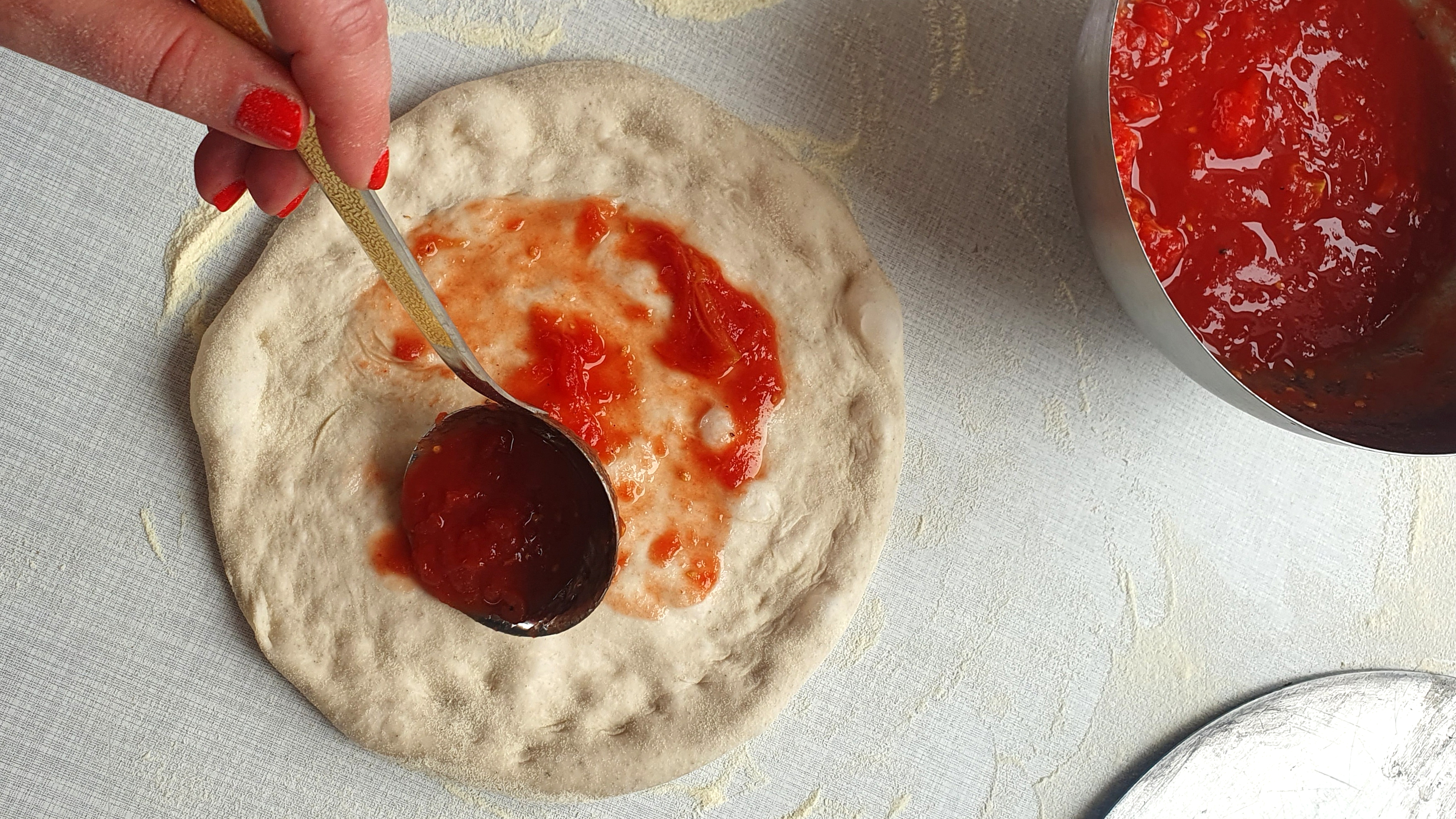 Roher Pizzaboden wird mit Tomatensauce bestrichen