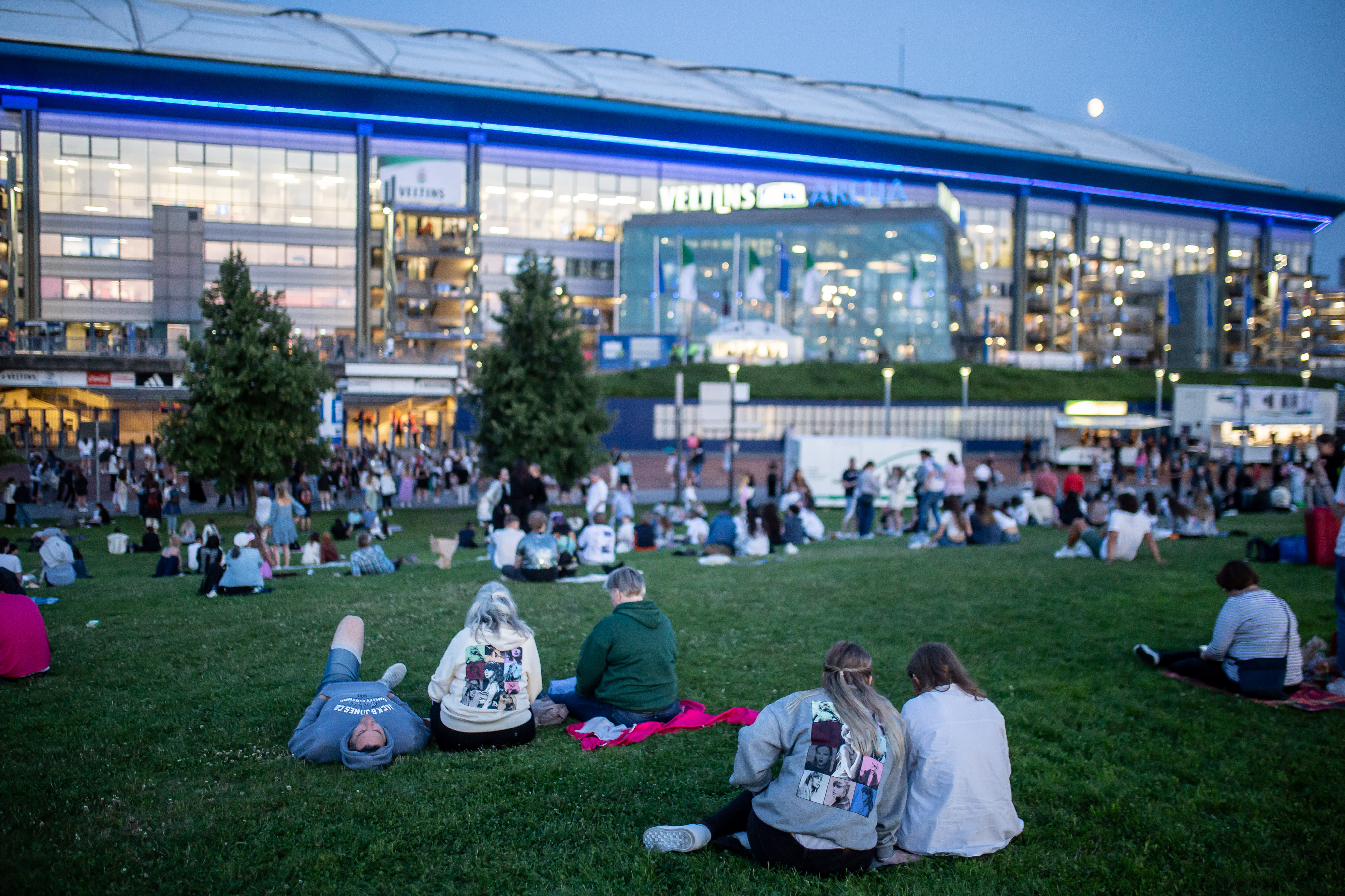 Menschen sitzen in der Abenddämmerung vor einem Stadion.