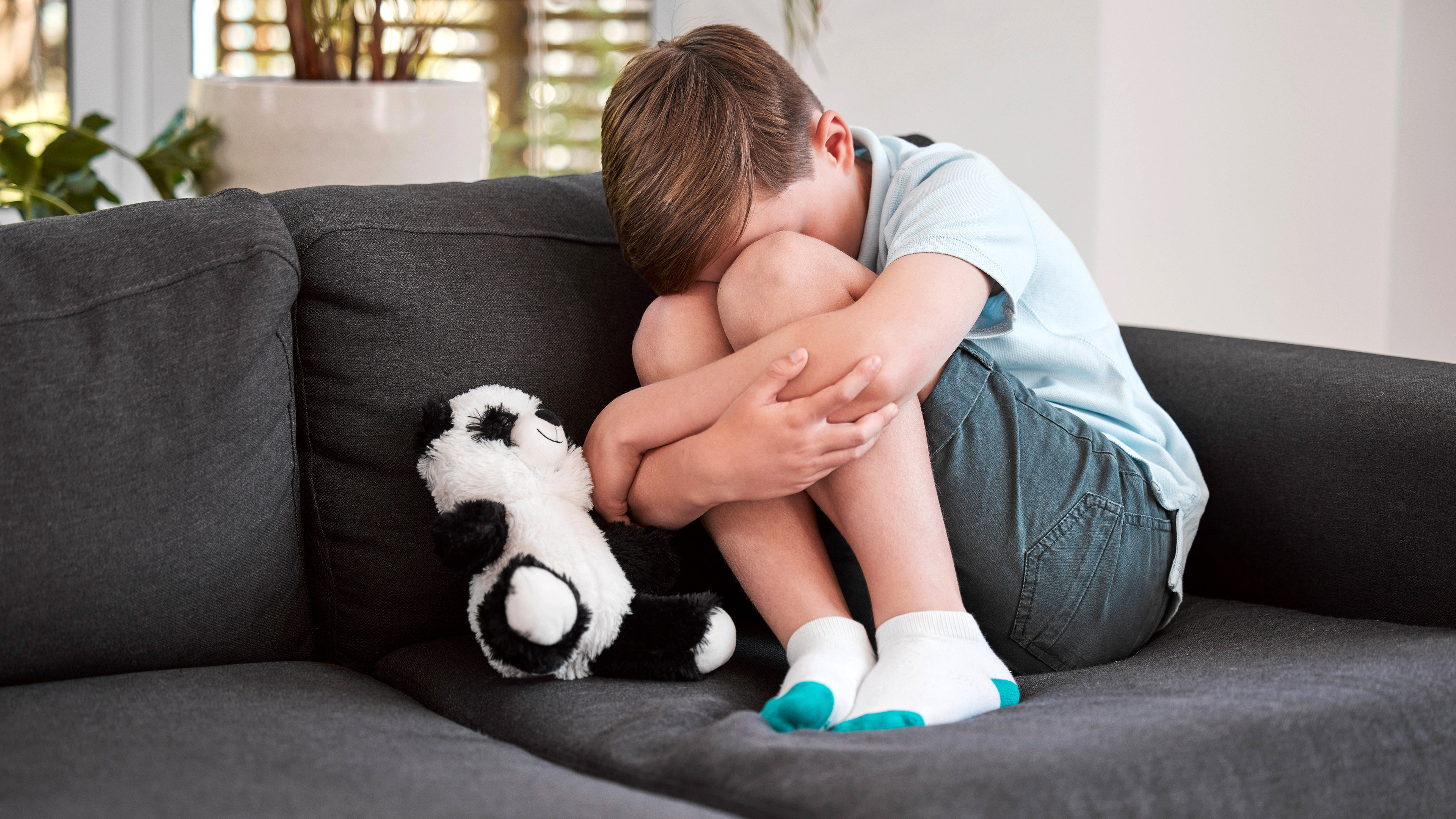 Junge sitzt traurig zusammengekauert auf dem Sofa