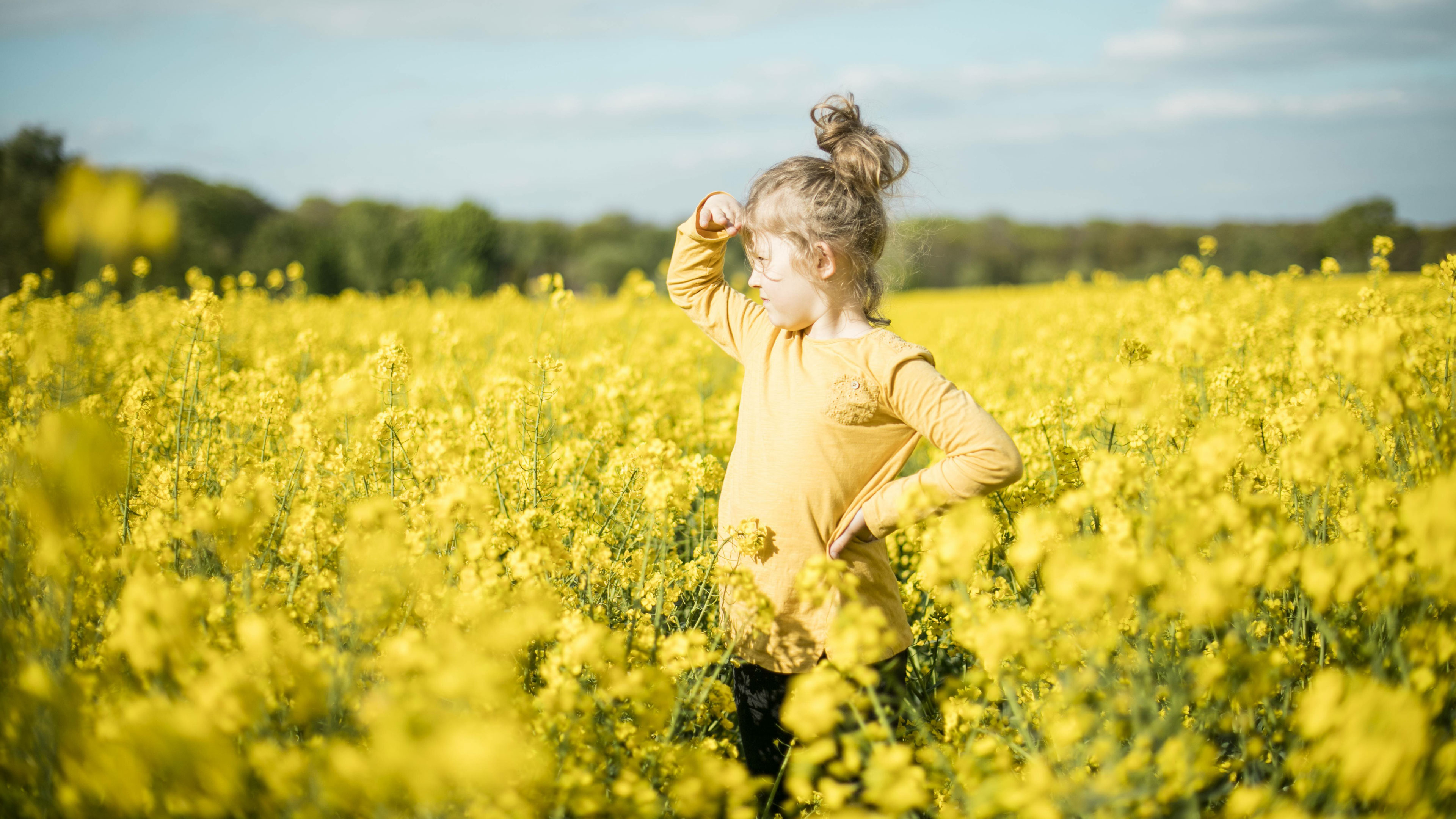 Ein Mädchen steht mitten in einem gelben Rapsfeld und schaut in die Ferne.