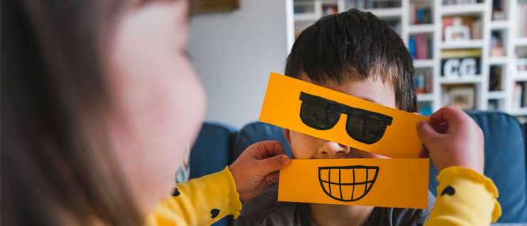 Kind hält anderem Kind aufgemalte Brille und Mund vor das Gesicht