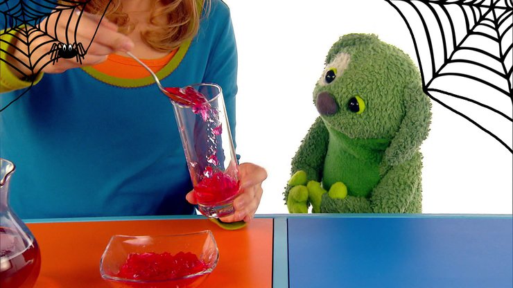 Tanja gibt roten Wackelpudding mit einem Löffel in ein Glas.