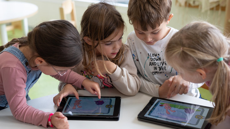 Vier Kinder mit zwei Tablets am Tisch