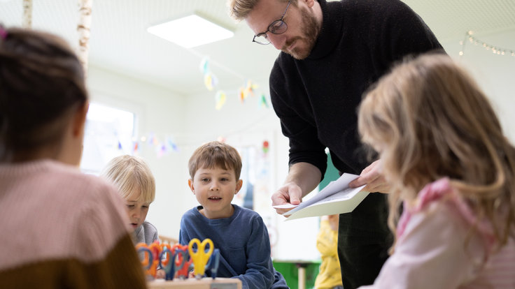 Lehrer verteilt Arbeitsblätter an vier Kinder