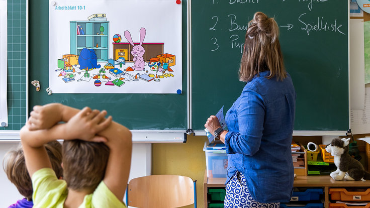 Lehrerin steht an der Tafel mit dem Arbeitsblatt vom Lernspiel 9 